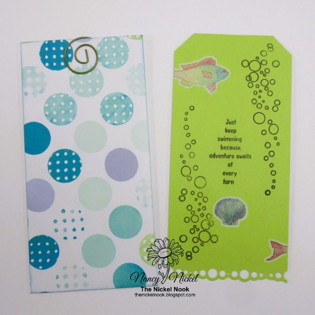 A decorative envelope with a teal, mint, and purple circular pattern on the left, secured by a spiral clip, and a vibrant green tag on the right featuring a fish graphic and an encouraging quote surrounded by bubble designs.