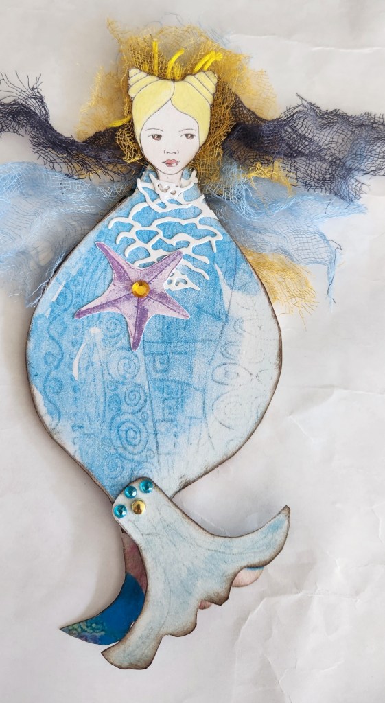 A whimsical mermaid notepad featuring a hand-drawn mermaid design with a blue and yellow palette, adorned with a starfish and decorative embellishments.