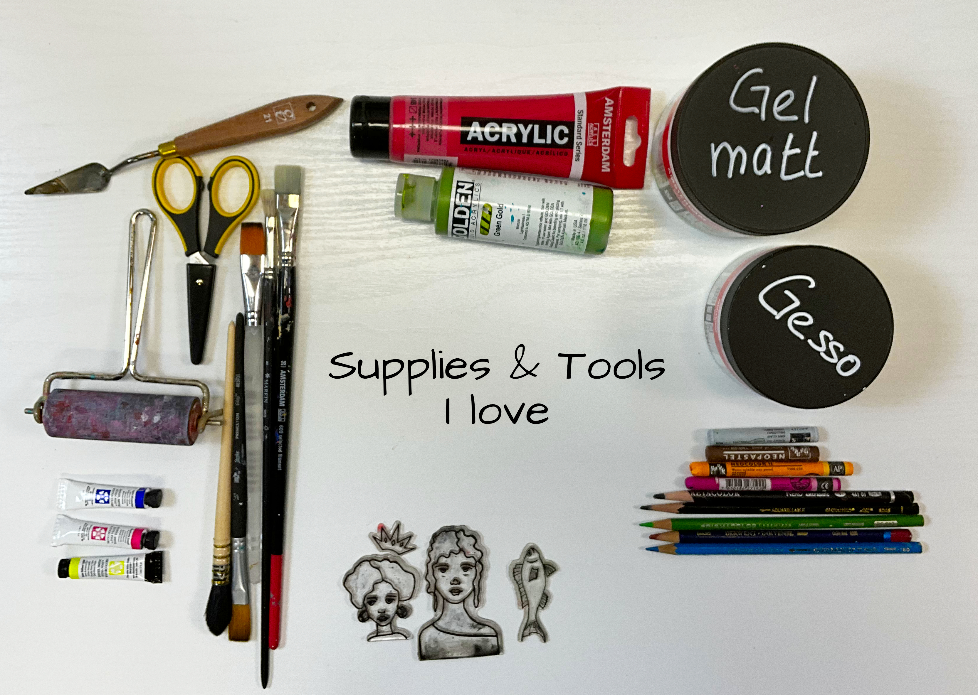 Bea Grob’s favorite mixed media art supplies including acrylic paints, gesso, gel medium, brushes, pencils, a brayer, and hand-drawn face stamps — flat lay on light wood background.