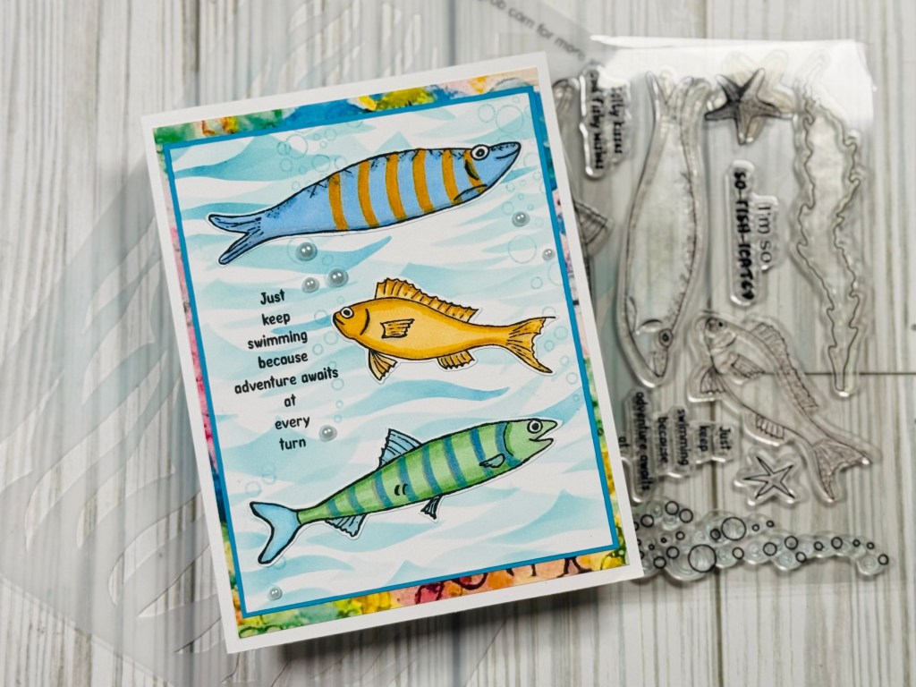 handmade card placed beside the clear stamp set used, showing stamped and colored fish with a background created using ocean-themed stencils and papers.