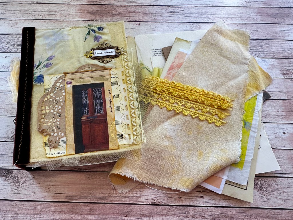 A mixed media art journal cover titled 'Golden Threads' featuring a decorative door image, lace, and various textured yellow fabrics on a wooden background.