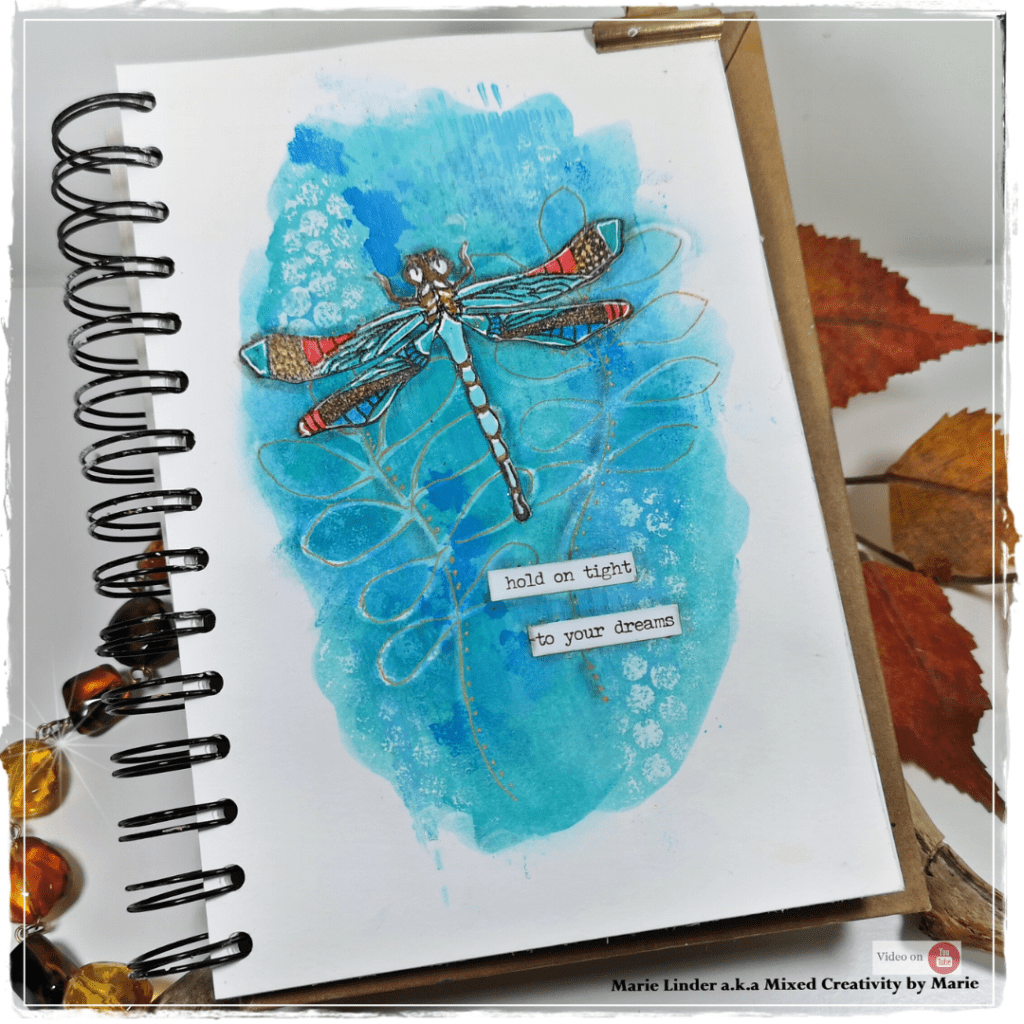 A bright and colorful art journal page featuring a dragonfly, decorated with watercolor-like blue backgrounds, stencils, and the quote 'hold on tight to your dreams'.
