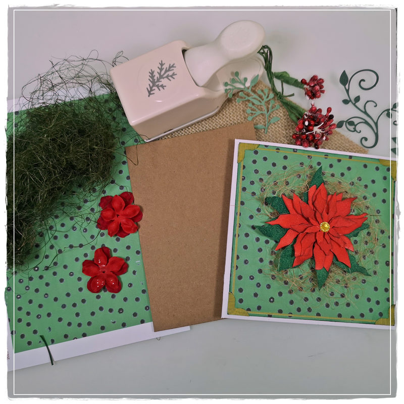 A festive handmade card featuring a red poinsettia flower, surrounded by green dotted paper and layered embellishments, alongside craft supplies including a kraft card base, floral decorations, and a decorative punch.