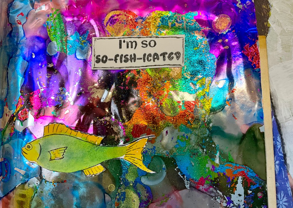 A colorful journal page featuring a vibrant, abstract background with swirls of purple, blue, and green. A cartoon fish is illustrated in bright yellow and green at the bottom, with a label in the center that reads 'I'm so so-fish-icated'.