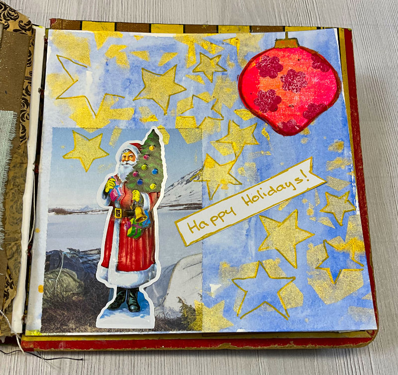 Art journal page featuring a cheerful Santa with a Christmas tree, colorful stars, and a red bauble on a soft blue watercolor background. The text 'Happy Holidays!' is also visible.