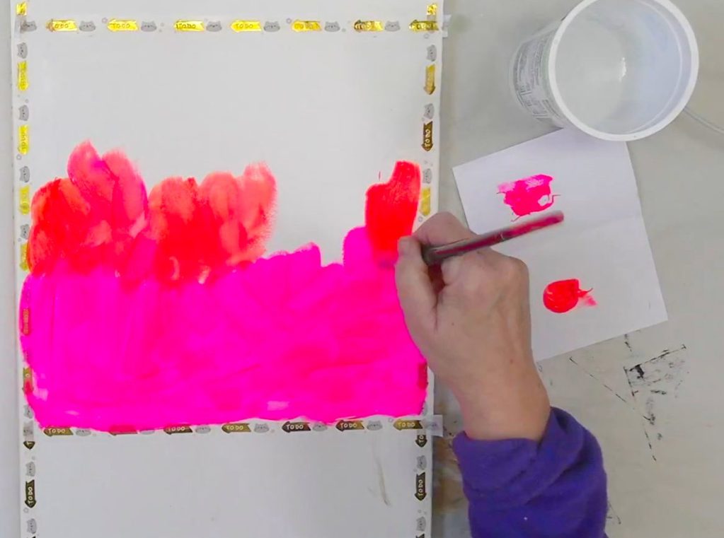 A hand painting a vibrant fluorescent pink background on a large art journal page.