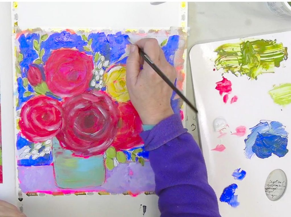 An artist paints a vibrant mixed media flower bouquet in a large A3 Moleskine Art Journal with a fluorescent background. Colorful acrylic paints and charcoal pencil tools are visible.