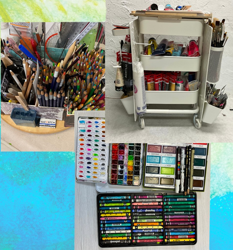 An assortment of art supplies including colored pencils, watercolor palettes, and tubes of acrylic paint organized on a cart and surfaces.