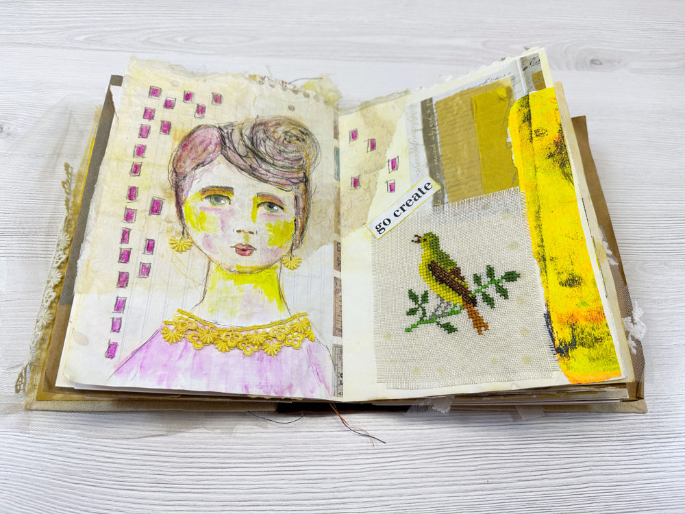 Mixed media journal spread featuring a hand-drawn portrait with yellow and purple shading, collage papers, and a stitched bird on fabric.