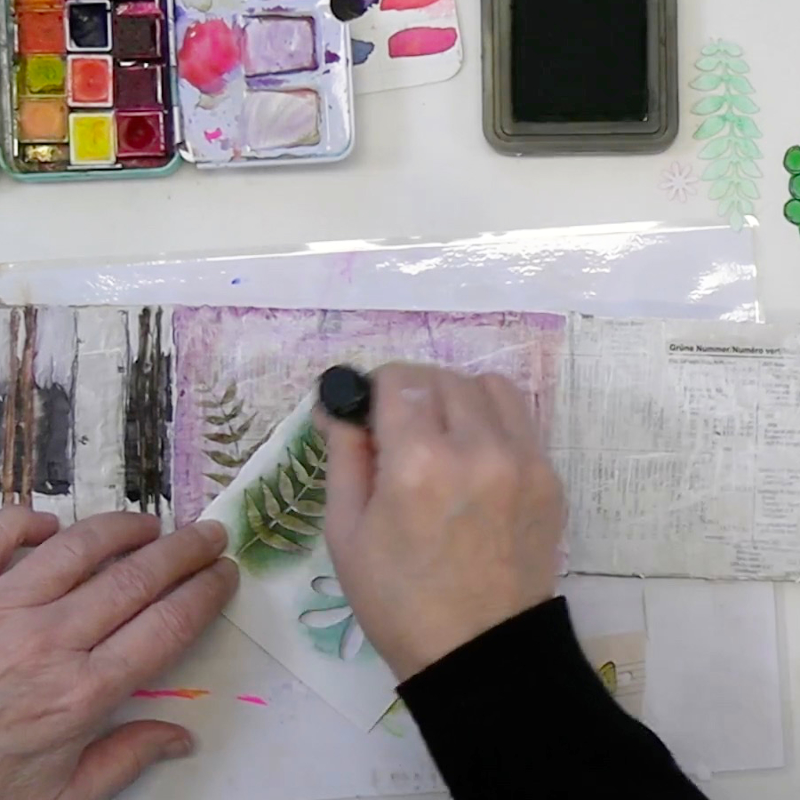 A person using a black marker to trace leaves on paper, surrounded by watercolor paints and other art supplies.
