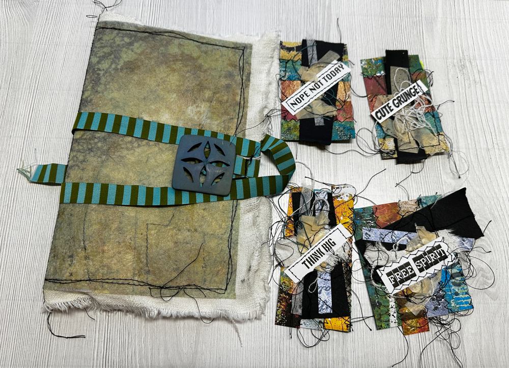 Handmade fabric art journal with Lutradur cover, striped ribbon closure, stitched binding, and small mixed media scrap embellishments made from collage paper and fabric