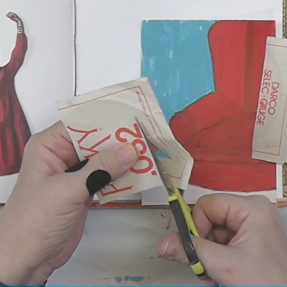 A person with a black glove is cutting a piece of paper in front of an open sketchbook displaying colorful artwork.