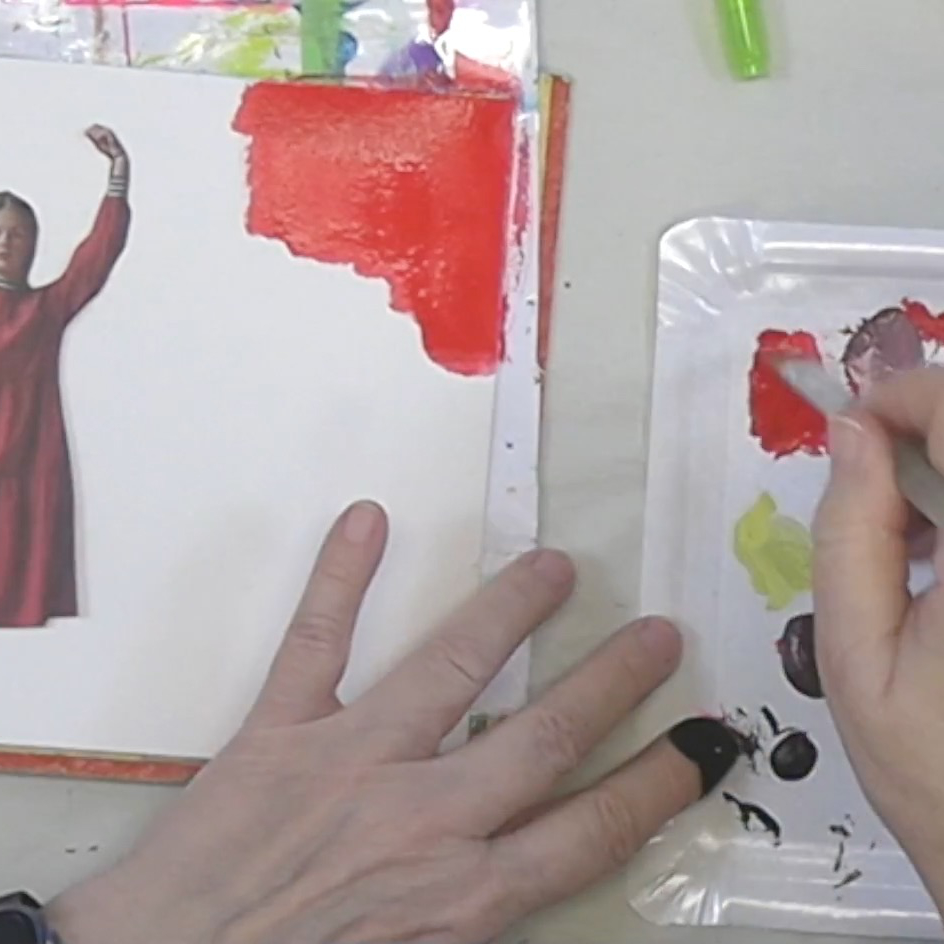 An artist's hand holding a paintbrush, working on a red area of a canvas, with a colorful palette and images in the background.