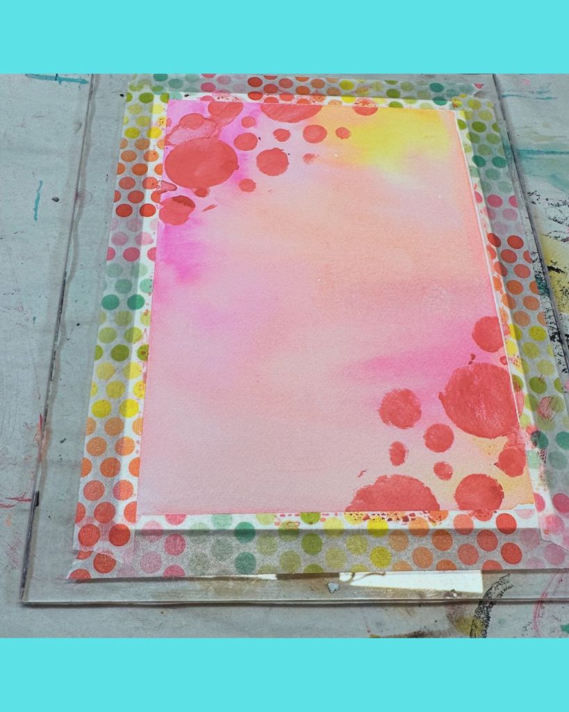 A watercolor painting with a soft pink background, featuring splashes of orange and yellow, bordered by a colorful polka dot tape.