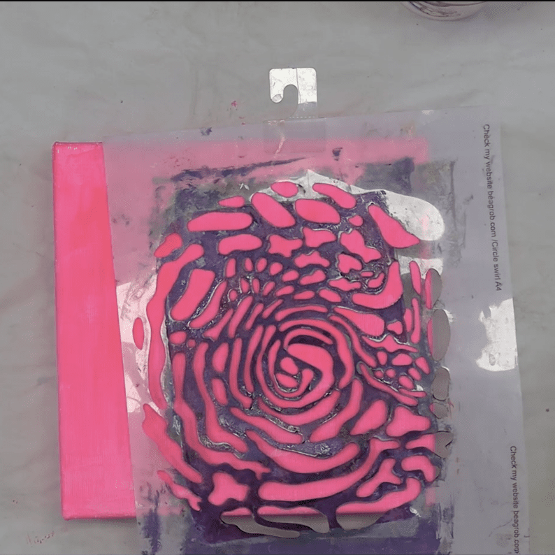 An artistic arrangement featuring a pink and purple swirl pattern created with a stencil on a white surface.