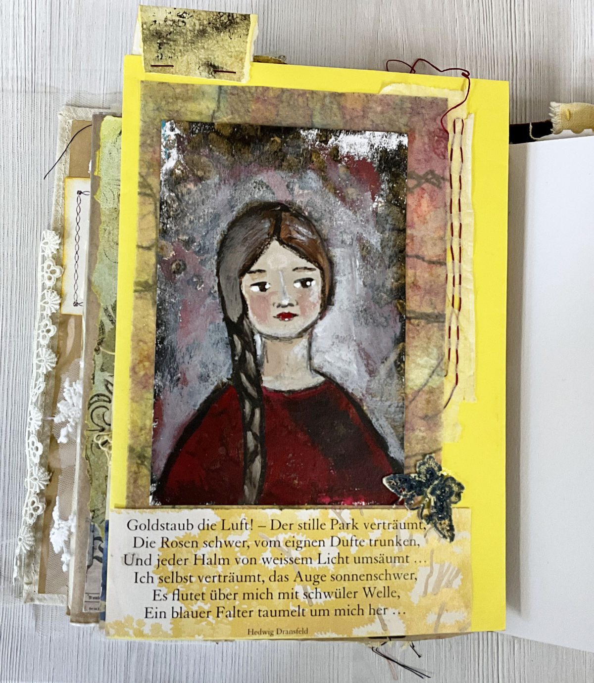 Art journal page featuring a painted portrait of a girl with a long brown braid and red dress, mounted on a yellow card with a textured collage background in ochre, gold and muted purples. Below the portrait, a poem by Hedwig Dransfeld in German, beginning "Goldstaub die Luft." A small decorative butterfly embellishment sits at the lower right. Part of the Golden Thread Journal.