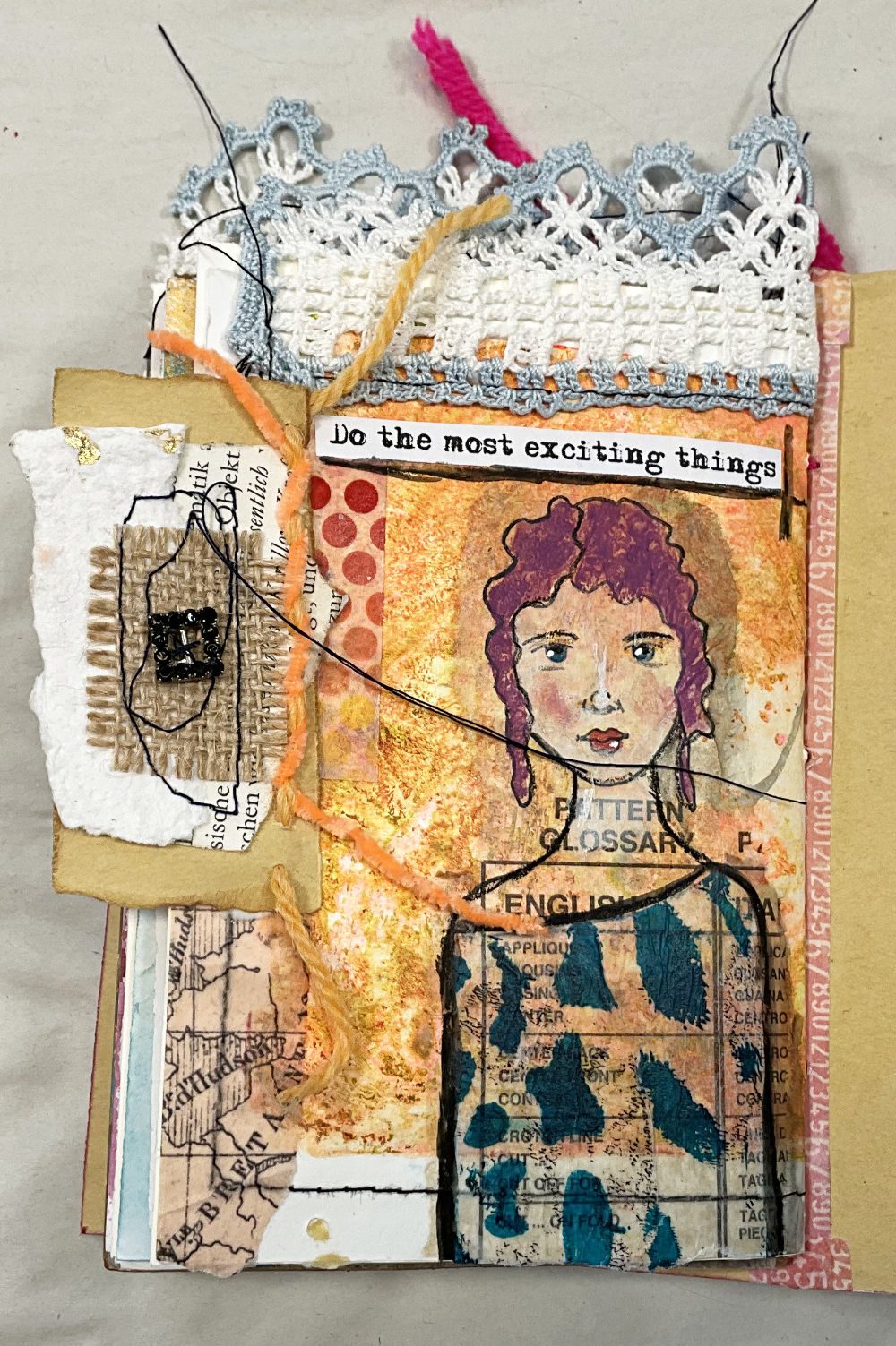 Handmade art journal page in orange tones featuring a stamped mixed media face, crochet lace border, and layered collage elements.